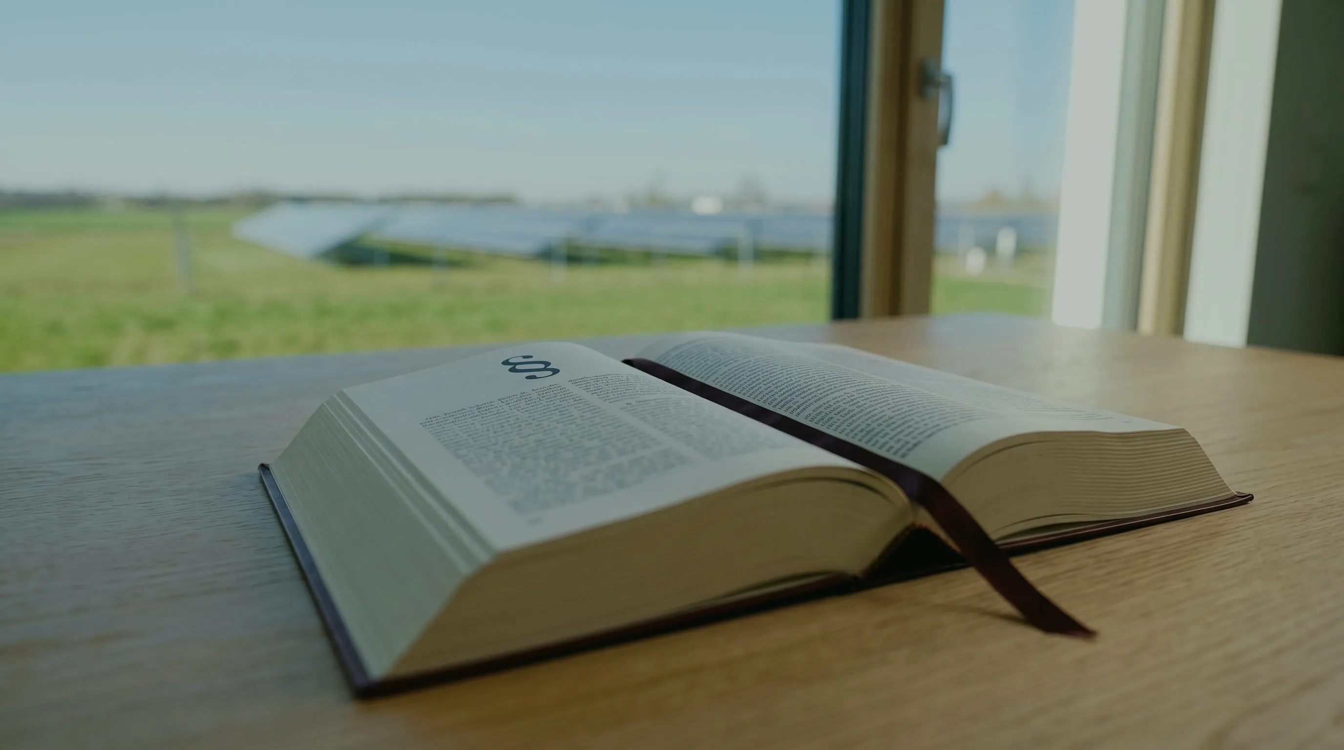 Investitionsabzugsbetrag nach § 7g EStG: aufgeschlagenes Gesetzbuch mit Paragrafenzeichen und Lesebändchen auf einem Holztisch am Fenster