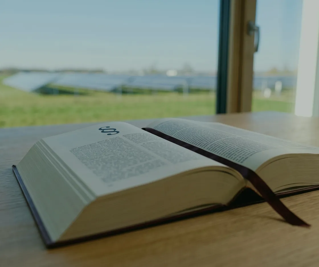 Investitionsabzugsbetrag nach § 7g EStG: aufgeschlagenes Gesetzbuch mit Paragrafenzeichen und Lesebändchen auf einem Holztisch am Fenster