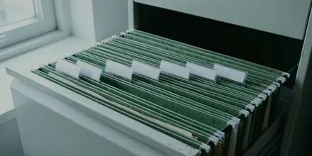 Geöffnete Schublade eines Aktenschranks mit grünen Hängemappen und leeren Beschriftungsreitern