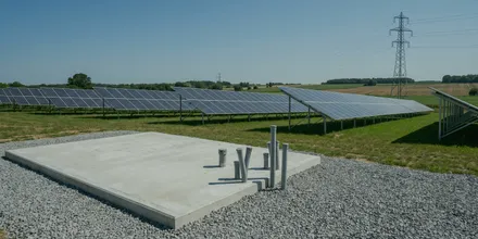Leeres Betonfundament mit vorbereiteten Kabelrohren am Rand einer Solaranlage, im Hintergrund ein Strommast