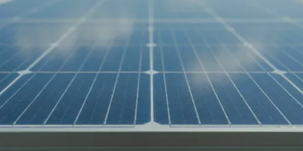 Nahaufnahme der Oberfläche eines Solarmoduls mit Zellstruktur und gespiegelten Wolken