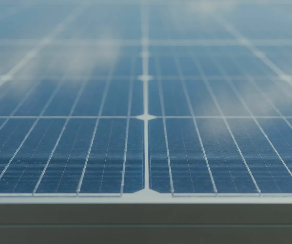Nahaufnahme der Oberfläche eines Solarmoduls mit Zellstruktur und gespiegelten Wolken