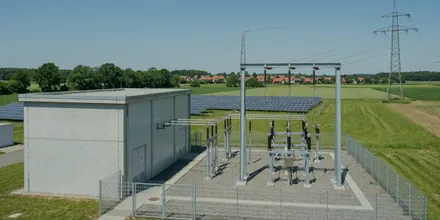 Umspannstation mit Schaltanlage und Betongebäude am Rand einer Solaranlage, dahinter ein Strommast