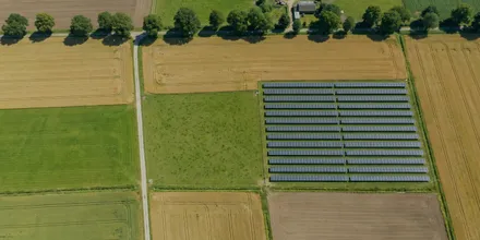 Senkrechtes Luftbild einer Feldflur, in der eine einzelne Solaranlage wie eine Parzelle zwischen den Ackerschlägen liegt
