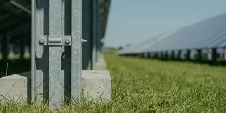 Nahaufnahme eines Stützfußes auf seinem Betonfundament im Gras, dahinter die Modulreihe