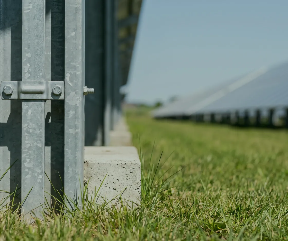 Nahaufnahme eines Stützfußes auf seinem Betonfundament im Gras, dahinter die Modulreihe
