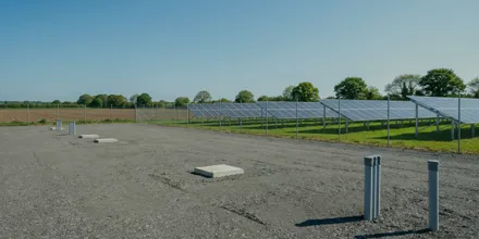 Freie Schotterfläche mit vorbereiteten Fundamenten und Pollern neben einer Solaranlage